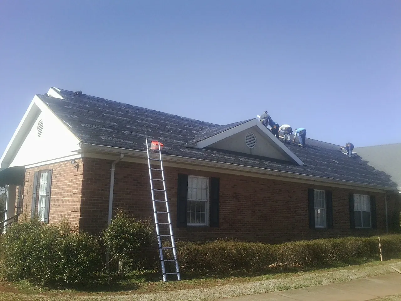 Crew tearing shingles off a brick ranch roof with a ladder set — Emergency Roof Repair work by our crew in Ridley Park