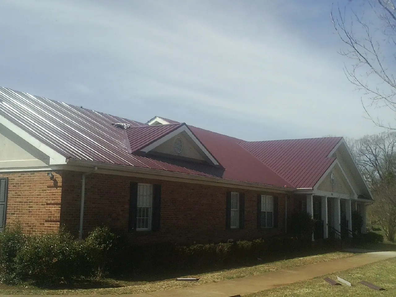 Red metal roof with gabled entries on a long brick building, from a Hail Damage Roof Repair job in Ridley Park