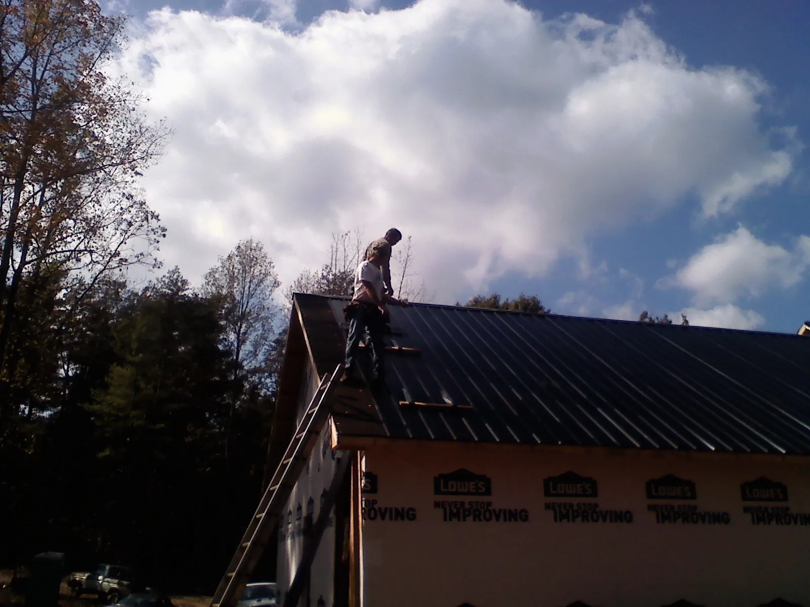 Roofer fastening dark metal panels high against a cloudy sky, from a Roof Inspection job in Ridley Park