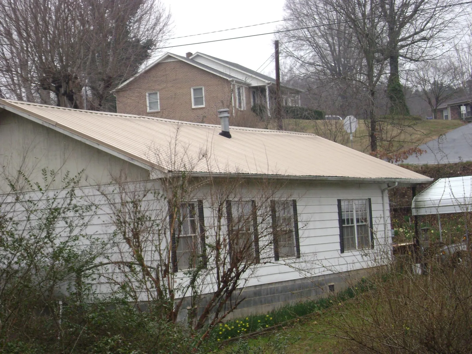Tan metal roof on a white sided house set into a hillside — Commercial Roofing by Roofing Brothers in Ridley Park